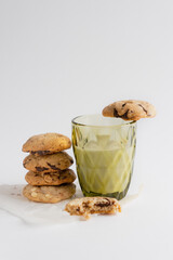 Homemade cookies with chocolate pieces next to a glass of milk on a white background