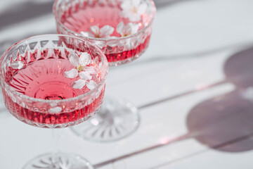Two fashionable glasses for dessert and champagne with a pink drink and cherry blossoms inside on a...
