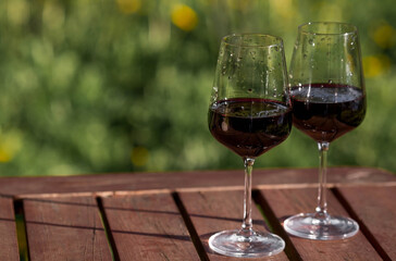 Two glasses of wine on a wooden table on the veranda with hard shadows and glare from the sun. The...