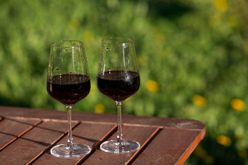 Two glasses of wine on a wooden table on the veranda with hard shadows and glare from the sun. The concept of a party and a holiday.