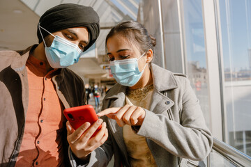 Indian couple wearing face masks using mobile phone in airport