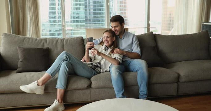 In modern skyscraper apartment pretty couple spend free time use smartphone, make video call enjoy pleasant talk. Young gen and wireless tech usage, make order, easy comfort e-services users concept