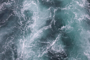 Water surface abstract background. White waves and foam on the blue sea water. Wake behind ship