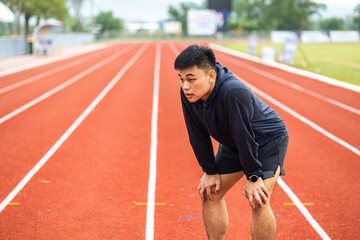 Fototapeta premium Young chinese man tired during jogging on the track in sport stadium. Young asian male intense training workout challenge breathing exhausted. Healthy and active lifestyle concept.