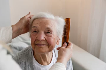 Foto op Plexiglas Unrecognizable female expressing care towards an elderly lady, brushing her hair with a comb. Granddaughter helping granny with a haircut. Family values concept. lose up, copy space, background. © Evrymmnt