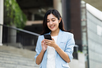 Beautiful business woman using mobile phone to play social media in the buildings at downtown. Smart female using cell phone chatting for business communication. Smartphone concept.