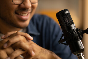 Young asian man host streaming podcast with condenser microphone work on laptop at small broadcast...