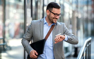 He never late. Smiling businessman looking at his watch on the way to office. Business, lifestyle concept