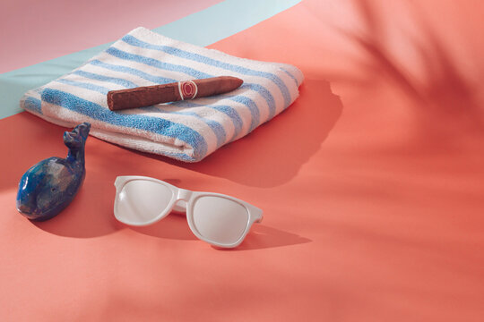 Sunglasses, blue and white towel, tompus and blue whale on coral background with shadows. Sun, summer, free space...