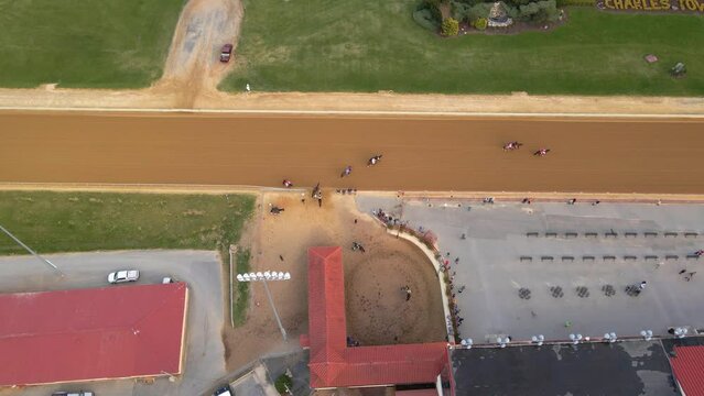 Aerial view of horse riders coming out from a stall to race on a track - birds eye, drone shot