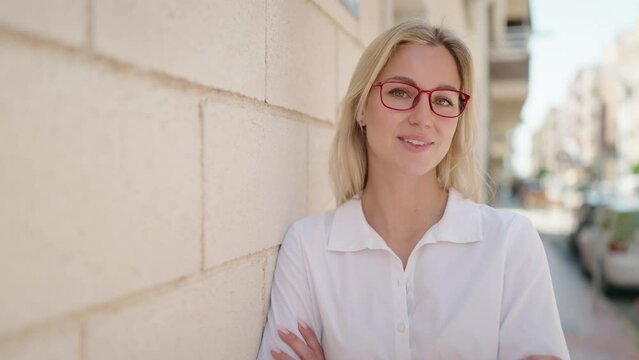 Young blonde woman smiling confident standing with arms crossed gesture at street