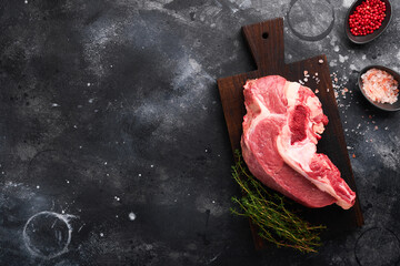 Raw beef meat. Rough piece of meat on bone for roast or soup with salt, pepper, thyme and rosemary on a black concrete background. Entrecote. Raw cowboy steak. Top view.