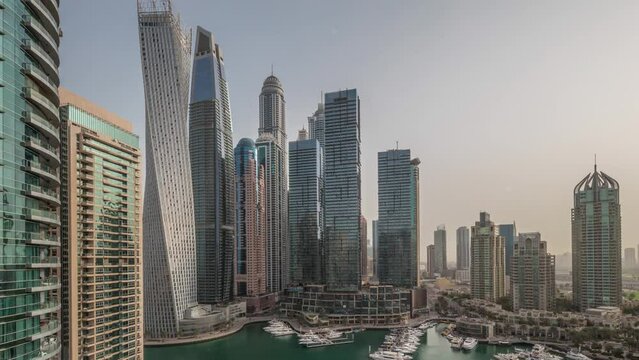 Dubai marina tallest skyscrapers and yachts in harbor aerial timelapse at morning with warm light. View at apartment buildings, hotels and office blocks, modern residential development of UAE