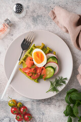 Savory waffles. Breakfast green waffles wild garlic or spinach with egg, tomato, salmon on plate for breakfast on grey concrete table background. Light dinner, lunch or breakfast. Top view. Mock up.