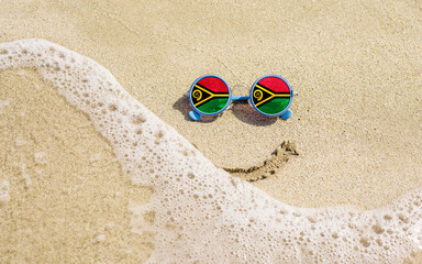 A painted smile on the sand and sunglasses with the flag of Vanuatu. The concept of a positive and successful holiday in the resort of Vanuatu.