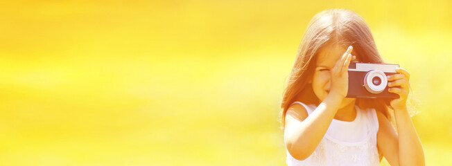 Portrait of little girl child with film camera taking picture on sunny summer background, banner...