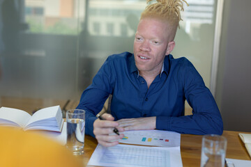 African american mid adult albino businessman looking away while working on graphs at desk in office
