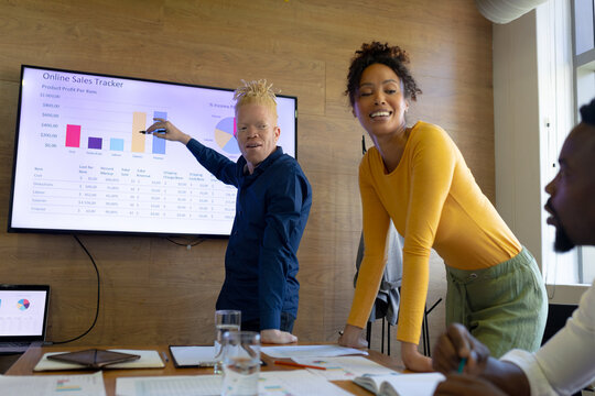 African american albino businessman showing graph on screen to mid adult colleagues in office - Powered by Adobe