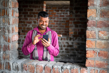 Happy smiling young indian labour busy on mobile phone at workplace - concept of using social media...