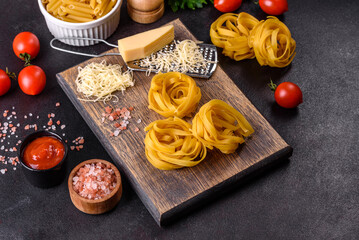 Raw tagliatelle paste with grated cheese, cherry tomatoes, spices and herbs on a wooden cutting board