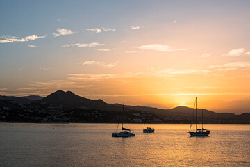 Fototapeta na wymiar Summer sunrise, with mountain skyline and small sailing boats at anchor. Golden sunlight with light cirrus clouds. Costa del Sol, Malaga, Spain.