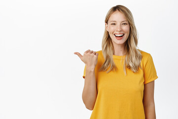 Portrait of happy smiling cute girl, woman pointing finger left at copy space, logo banner, company advertisement, standing against white background