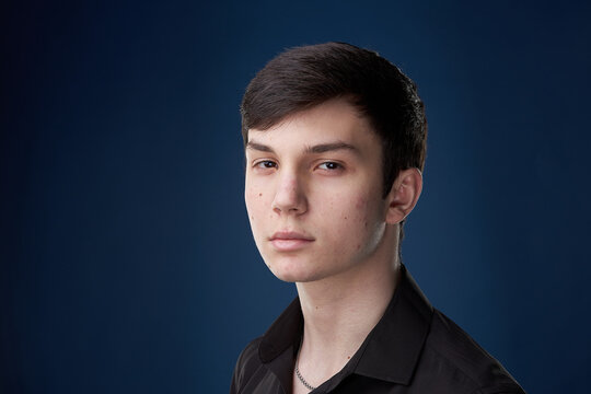 Portrait of a brunette teenager, in a black shirt on a navy blue background.