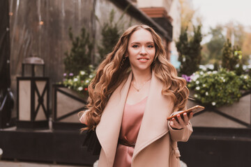 Beautiful young woman with long hair and in coat walks around the city and writes message on the...