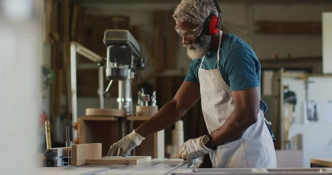 African american male carpenter using table saw for cutting wood at a carpentry shop