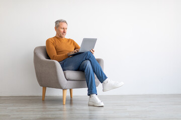 Confident mature man using laptop sitting on chair - Powered by Adobe