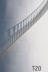 Sunlight and shadow on surface of curve spiral staircase on white oil storage fuel tank in vertical...