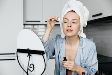woman applying moisturising serum to face and looking to mirror at home in the kitchen
