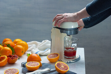 Woman Squeezing Blood Oranges in Vintage Juicer to Make Fresh Orange Juice
