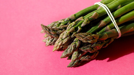 a bunch of fresh green asparagus lies on a pink background. a place to copy. vegan. healthy food....