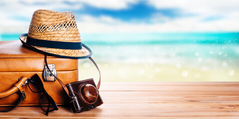 Vintage suitcase, sunglasses and hipster hat wooden deck and blur tropic sea background. Summer...