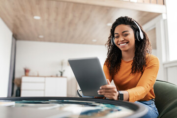 Smiling black woman in headset using tablet in living room