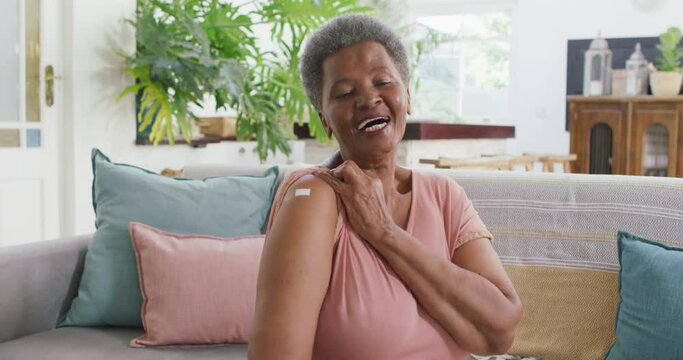 African american senior woman showing the band aid on her shoulder sitting on the couch at home