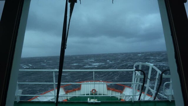 Vessel in storm. Bow breaks wave. Splashes of water. View from bridge. High waves. Strong pitching. White foam on water.