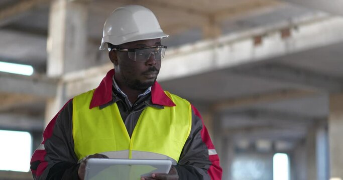 African american builder manager of the works stands at construction site and makes notes in tablet computer. Cinema 4K 60fps video