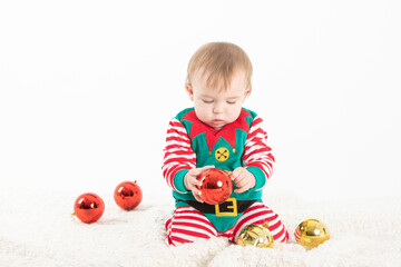Fototapeta na wymiar baby in elf costume grabbing christmas balls with serious expression