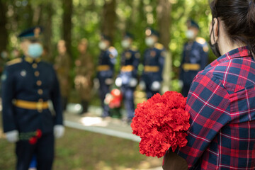 Flowers on memorial. Funeral of soldier. Girl at military ceremony. Red flowers in hands of woman.