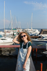 Fototapeta na wymiar A smiling girl with sunglasses is on the pier waiting for the boat