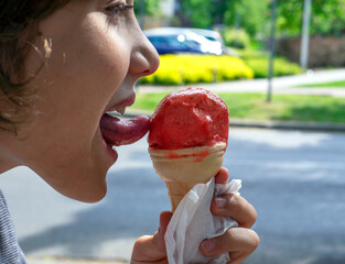 smiling boy licks strawberry natural ice cream with his tongue on a walk on a sunny day in profile...