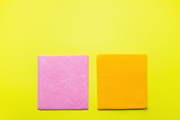 top view of bright pink and orange dishrags on yellow background.