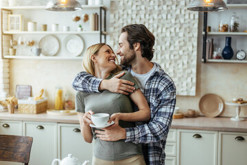 Smiling caucasian millennial male with stubble hugs blonde female, drink coffee, enjoy tender moment