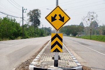 Yellow warning road sign with symbol of arrows on the road  for the two way run  in rural of Thailand.        