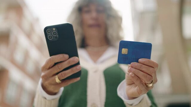 Middle age woman using smartphone and credit card at street
