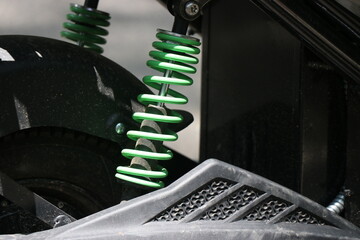 The green shock absorber of the electric scooter parked outside with a closeup of springs that...