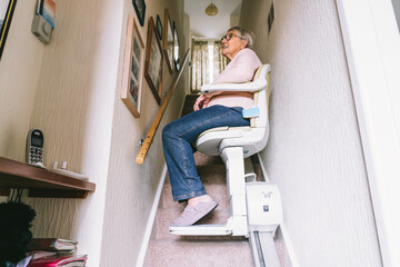 Senior woman using automatic stair lift on a staircase at her home. Medical Stairlift for disabled...