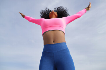 African-American woman with afro hair and sportswear, with fluorescent pink t-shirt and leggings,...